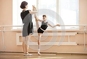 Ballet teacher adjusting leg position of young ballerinas