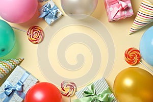 Balloons, gift boxes, lollipops and birthday hats on color background