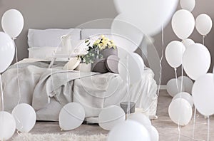Balloons in industrial stylish bedroom with grey bedding, trey and round boxes with flowers on th bed