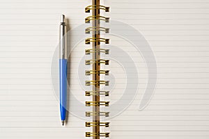 Ballpoint pen made of blue plastic and metal standing on lined notebook