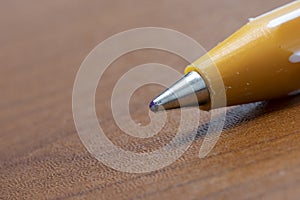 Ballpoint pen nib close-up. It is yellow and brown on the table