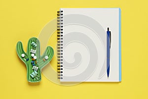 Ballpoint pen, notebook and different clips on yellow background, flat lay