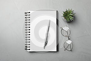 Ballpoint pen, notebook and glasses on light gray table, flat lay