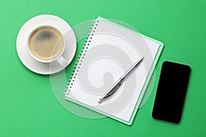 Ballpoint pen, notebook and smartphone on green background, flat lay