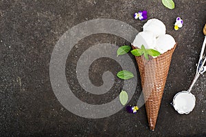 Balls of creamy vanilla ice cream in a crispy chocolate mug with edible viola flowers and mint leaves on a dark