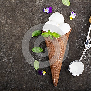 Balls of creamy vanilla ice cream in a crispy chocolate mug with edible viola flowers and mint leaves on a dark