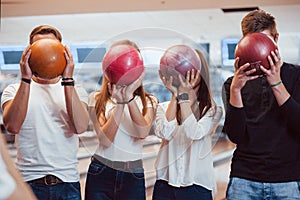 Balls with different numbers on it. Young cheerful friends have fun in bowling club at their weekends