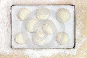 Balls of dough on parchment paper, on a metal tray on a wooden t