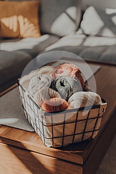 Balls of earth coloured yarn in a basket on a table inside an apartment