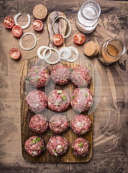 Balls of minced meat on a cutting board with cherry tomatoes and seasonings wooden rustic background top view close up