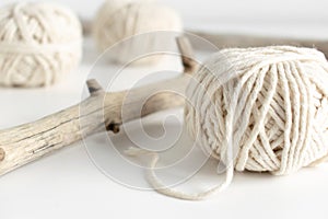 Balls of white yarn and rustic sticks on a white table. Threads of wool boho image.Good for macrame and handicrafts banners and