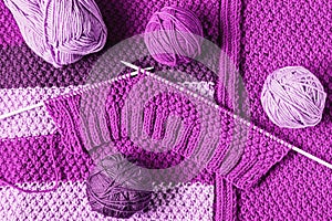 Balls of wool and unfinished knitting in violet tones, flat lay