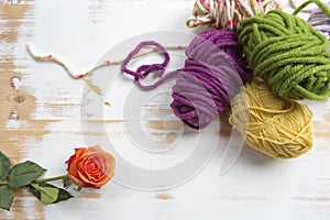 Balls of wool on wooden background with orange rose