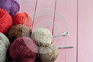 Balls of yarn in different colors with knitting needles on a background of pink wood texture.