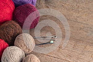 Balls of yarn in different colors with knitting needles on a background of rough wood texture.