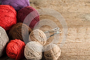 Balls of yarn in different colors with knitting needles on a background of rough wood texture.