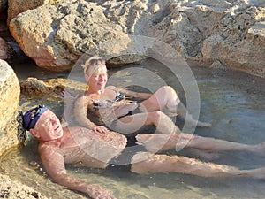Balneotherapy, a man and a woman lie in a natural mineral water between stones in the sunlight
