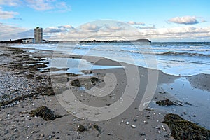 Baltic sea beach with blue waves, wet sand, algae, pebbles and the hotel tower of travemuende in the background under a blue sky