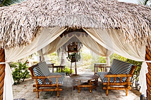 Bamboo benches with cushions, low round table are in an open thatched pavilion