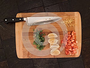 Bamboo cutting board with chef knife and prepared chives lemon zest and tomatoes