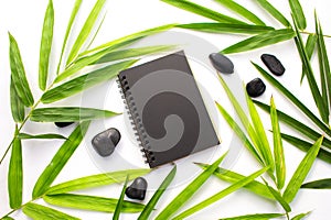 Bamboo leaf zen background. Black paper notebook mockup. Green bamboo leaf and beach pebbles flat lay.