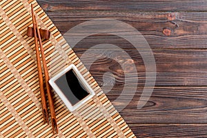 Bamboo mat and soy sauce with sushi chopsticks on wooden table. Top view with copy space background for sushi. Flat lay