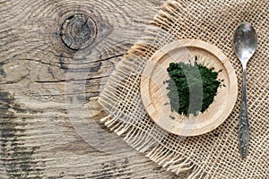 Bamboo plate with green chlorella powder with vintage spoon on canvas linnen napkin on wooden background, top view