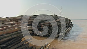 Bamboo poles tied together and pulled behind a small boat down the river (side view)