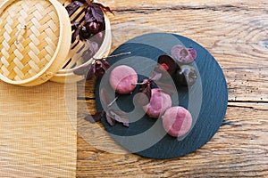 A bamboo steamer with cherries sits on a table next to a plate of food. Mochi asian dessert