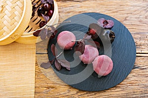 A bamboo steamer filled with cherries and plums rests on a wooden table. Mochi asian dessert