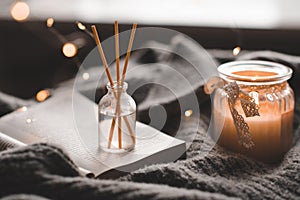 Bamboo sticks in bottle with scented candles and open book on wooden tray in bed closeup.