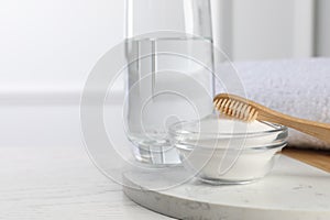 Bamboo toothbrush, bowl of baking soda and glass of water on white table, space for text