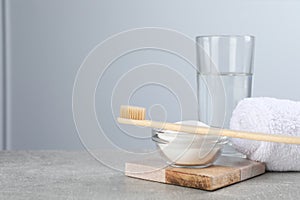 Bamboo toothbrush, bowl of baking soda, towel and glass of water on grey table, space for text