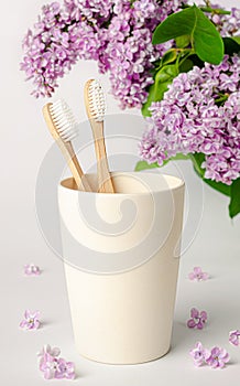 Bamboo toothbrush in eco cup with lilac flowers on white background. Zero waste and health care