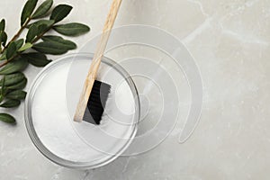 Bamboo toothbrush, glass bowl of baking soda and green leaves on light marble table, flat lay. Space for text