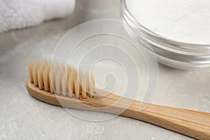 Bamboo toothbrush and glass bowl of baking soda on light grey marble table, closeup