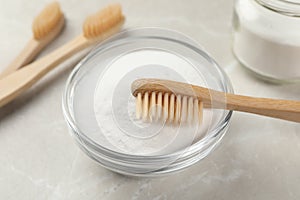 Bamboo toothbrush and glass bowl of baking soda on light table, closeup