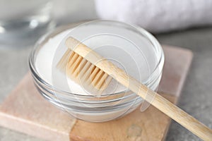 Bamboo toothbrush and glass bowl of baking soda on light table, closeup