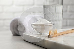 Bamboo toothbrush and glass bowl of baking soda on light table, space for text