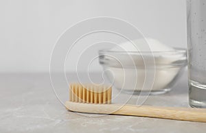 Bamboo toothbrush and glass bowl of baking soda on light table, space for text