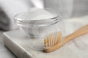 Bamboo toothbrush and glass bowl of baking soda on marble board, closeup. Space for text