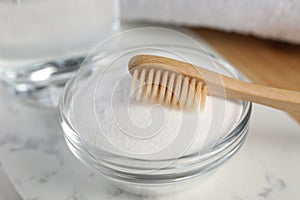 Bamboo toothbrush and glass bowl of baking soda on white marble table, closeup