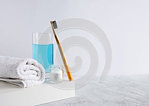 Bamboo toothbrush, glass of mouthwash, white a cotton towel and powder for brushing teeth in jar