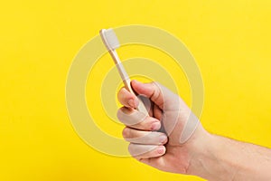 Bamboo toothbrush in hand on a yellow background, great for promoting eco friendly lifestyles or oral hygiene products.