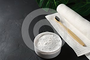 Bamboo toothbrush, tooth powder and white cotton towel on a black concrete background.