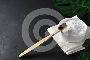 Bamboo toothbrush, tooth powder and white cotton towel on a black concrete background.