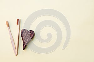 Bamboo toothbrushes and wooden heart on yellow background
