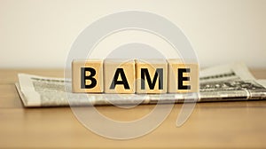 BAME symbol. Abbreviation BAME, black, asian and minority ethnic on wooden cubes on newspaper. Beautiful white background. Copy