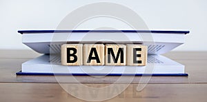 BAME symbol. Abbreviation BAME, black, asian and minority ethnic on wooden cubes in book. Beautiful white background. Copy space. photo