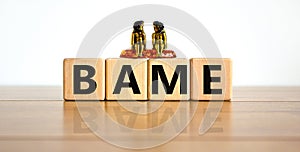BAME symbol. Abbreviation BAME, black, asian and minority ethnic on wooden cubes. Two metalic angeles. Beautiful wooden table, photo